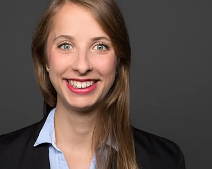 Lisa Kratochil hat langes mittelbraunes Haar, grüne Augen und ein strahlendes Lächeln. Sie trägt eine hellblaue Bluse und darüber einen dunklen Blazser.