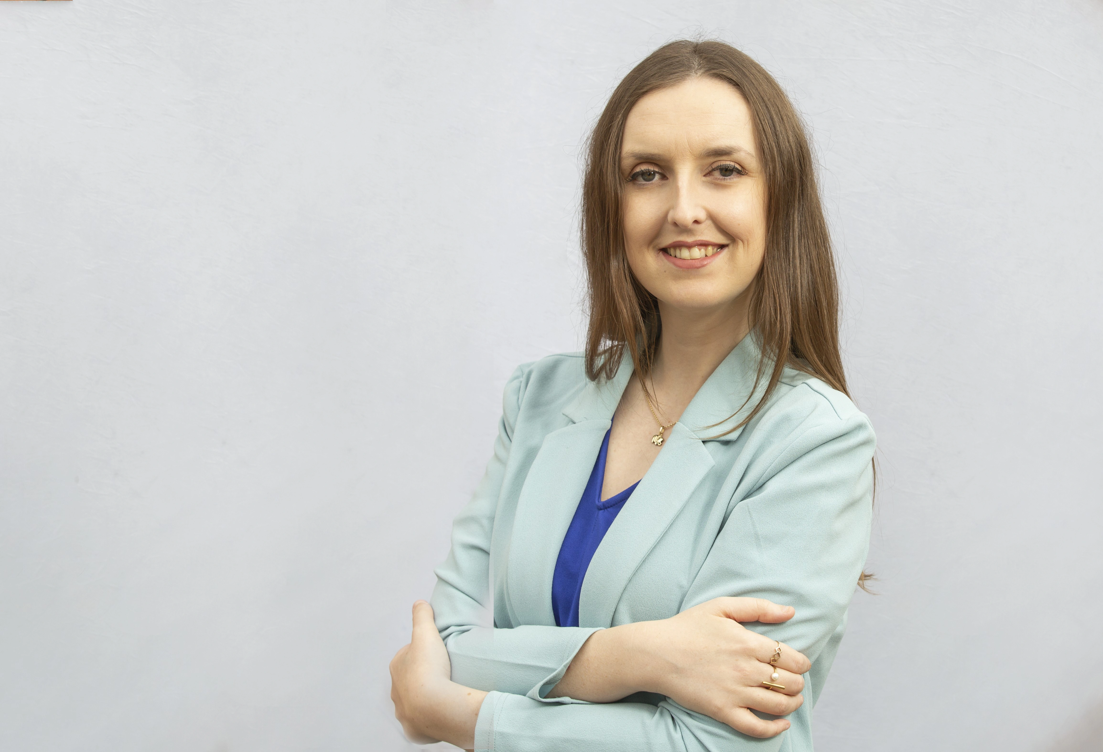 Jodie Brush lächelt in die Kamera. Sie hat langes hellbraunes Haar. Sie trägt ein mittelblaues Top und darüber eine sehr hellblauen Balzer.