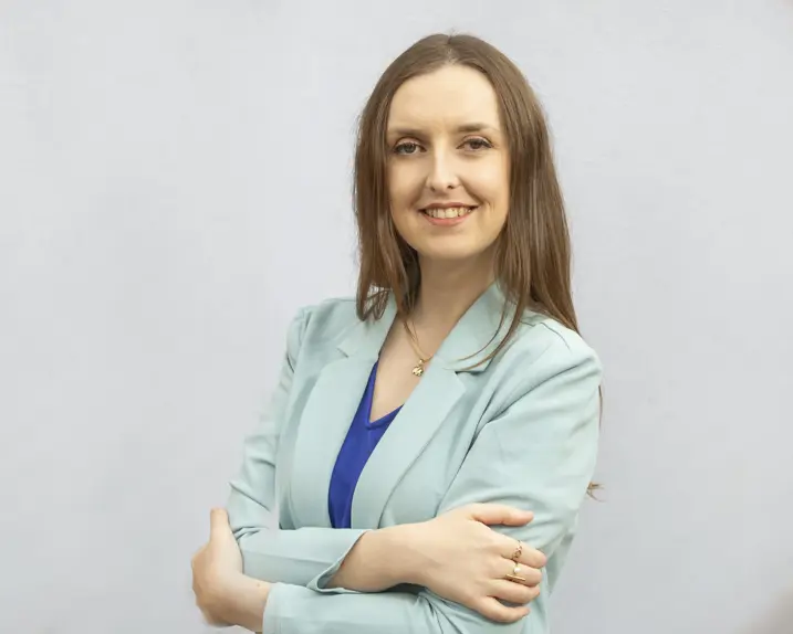 Jodie Brush lächelt in die Kamera. Sie hat langes hellbraunes Haar. Sie trägt ein mittelblaues Top und darüber eine sehr hellblauen Balzer.